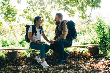 Cheerful multiracial friends sitting on bench in tree shade