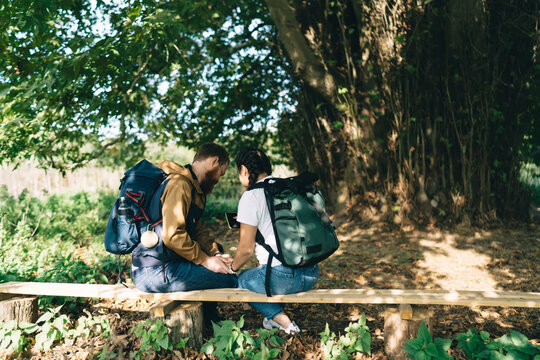 Trekking couple with backpacks resting on wooden bench