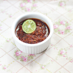 Sambal Bajak in white ceramic bowl with basil leaves on top. Sambal Bajak is a very famous chili sauce in Indonesia, Javanese Traditional food. ingredient consisting of chili, shallots, salt