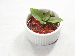 Sambal Bajak in white ceramic bowl with basil leaves on top. Sambal Bajak is a very famous chili sauce in Indonesia, Javanese Traditional food. ingredient consisting of chili, shallots, salt