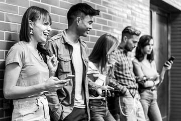 Multicultural friends laughing using smartphone at wall on university college campus - Young people...