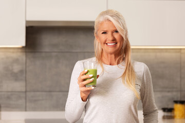 Beautiful, older woman drinking a healthy green - fruit and vegetable smoothie.