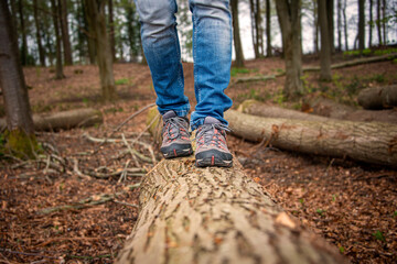 close up of a man walking along a log in the countryside.