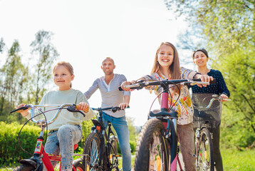 Smiling father and mother with two daughters during summer outdoor bicycle riding. They enjoy...