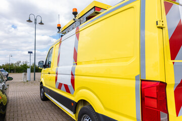 Yellow special cargo escort road traffic car roof mounted digital sign board. Repair and service van with ladder and orange light bar on roof at city street. Assistance or installation team vehicle