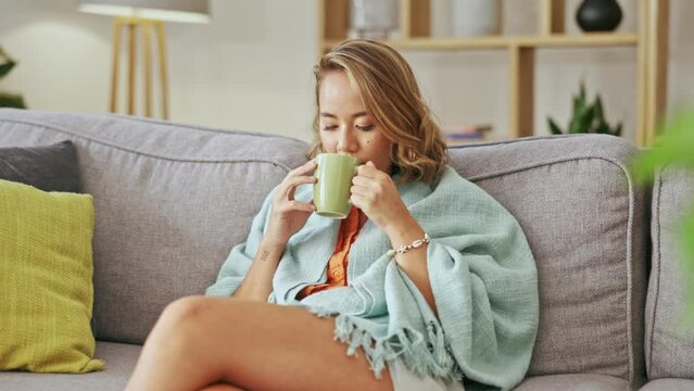 Happy asian woman drinking coffee on living room sofa for peace, calm mindset and easy lifestyle at home. Young female, relaxing and contemplating with tea, latte and hot cocoa on couch for self care