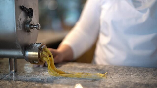 Front view of anonymous female chef making noodles using special pasta machine and spreading them along marble kitchen restaurant table