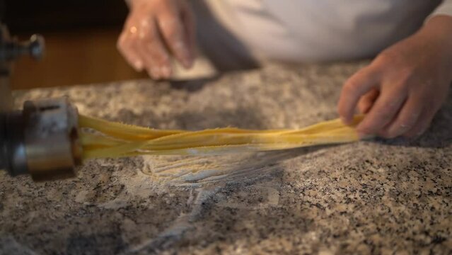 Anonymous female chef preparing long spaghetti noodles using professional pasta making machine and shaking and spreading noodles over the marble restaurant kitchen table