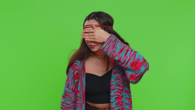 Nosy curious young woman closing eyes with hand and spying through fingers, hiding behind hand fingers, peeping gesture exploring way seeking something in distance. Girl on green chroma key background