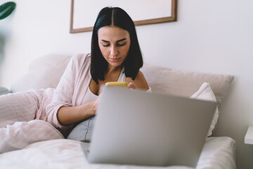 Happy woman with cellphone lying on bed