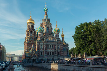 Fototapeta na wymiar A low angle shot of a river and people on an embankment in front of the Church of the Savior on Spilled Blood against a cupola by summer day