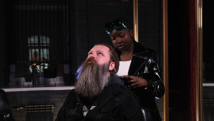 Fototapeta na wymiar African-American hairdresser girl prepares a man for a haircut in a barbershop.