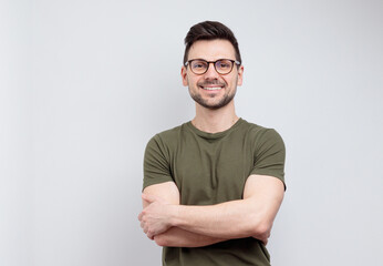 Smiling handsome man in t-shirt standing with crossed arms isolated on gray background