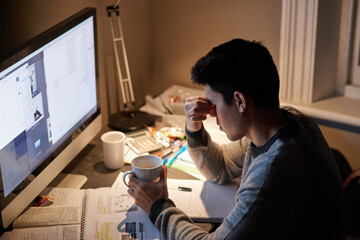 Man, studying and headache in night by computer for test, assessment or stress in college dorm room. Male university student, tea cup or burnout with anxiety, fatigue or tired with books for learning
