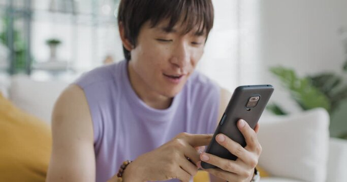 Gen Z Gay queer man non-binary pride at home. Asia LGBT young guy adult people happy relax sitting at sofa use omni channel easy buy now pay later BNPL shop store online bank loan. Cash sale discount.