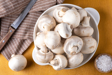 Close-up of champignon mushrooms on a white ceramic plate on a yellow background. Selective focus.