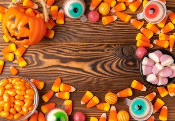 Halloween pumpkin-flavored corn candy, jelly eye, sugar skull and jelly beans on a brown background. Classic sweet Halloween treats. Halloween holiday concept and Jack lantern.Place for text. 