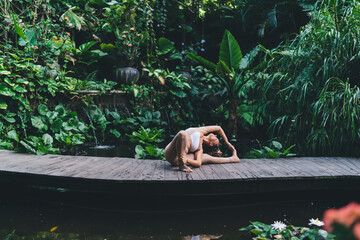 Active young woman with slim body doing asana pose during morning workout at nature pond, flexible female trainer enjoying active healthy lifestyle practicing hatha yoga reaching body positive