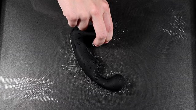 A woman holds a black prostate stimulator that vibrates and creates ripples on the surface of the water. Switch different modes. 