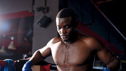 African male boxer is standing in the corner of a boxing ring preparing to meditate for the next...