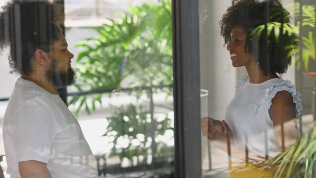Two happy friendly young diverse business people talking during work break standing in office, employees share ideas enjoy conversation discussing team project at meeting
