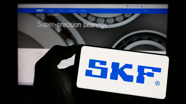 Stuttgart, Germany - 04-28-2023: Person holding cellphone with logo of Swedish bearing manufacturing company SKF AB on screen in front of webpage. Focus on phone display.