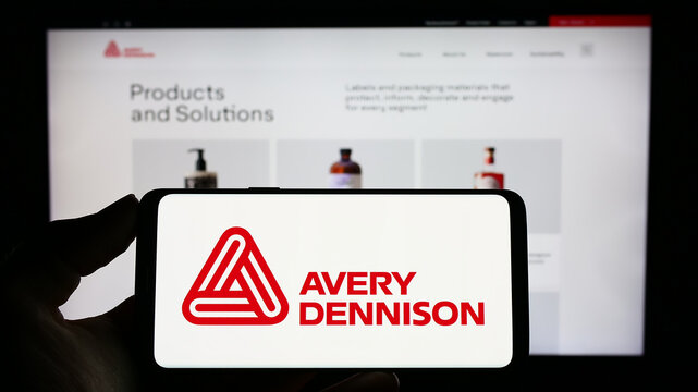 Stuttgart, Germany - 04-28-2023: Person holding cellphone with logo of American packaging company Avery Dennison Corporation on screen in front of webpage. Focus on phone display.