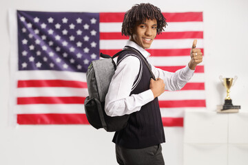 African american male student looking over shoulder and gesturing thumbs up with the usa flag in the back