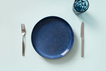 Empty navy blue plate and glass for water on blue background. Kitchen and cooking template, mock...