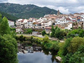 View of the town of Ribadavia in Orense, reflected in the Avia river, on a cloudy day, with the bell tower and white houses, in the background the mountain in summer of 2021 Spain