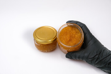 A hand in a black glove holds an open jar of pike caviar on a white background. Healthy food concept.