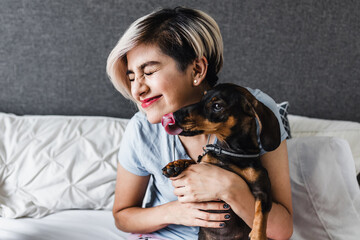 latin young woman with dog dachshund pet on bed at home in Mexico Latin America, hispanic female 
