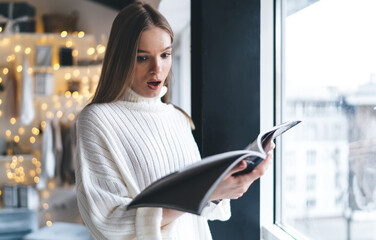 Young female reading shocking news in magazine