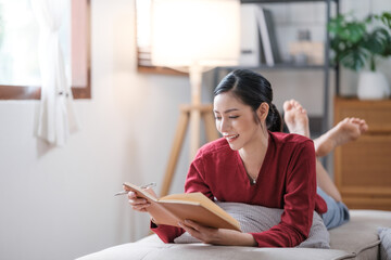 Naklejka premium Asian woman woman reading book sitting on sofa in living room.