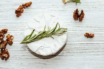 Round cheese in camembert mold with a sprig of rosemary on the table.