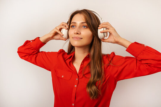 Beautiful blonde woman wearing red shirt is wearing headphones on her head over grey background.