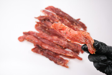 Dried pork isolated on white background. Pieces of dry meat in the hand of a chef in a black glove. Beer snack. Close-up.