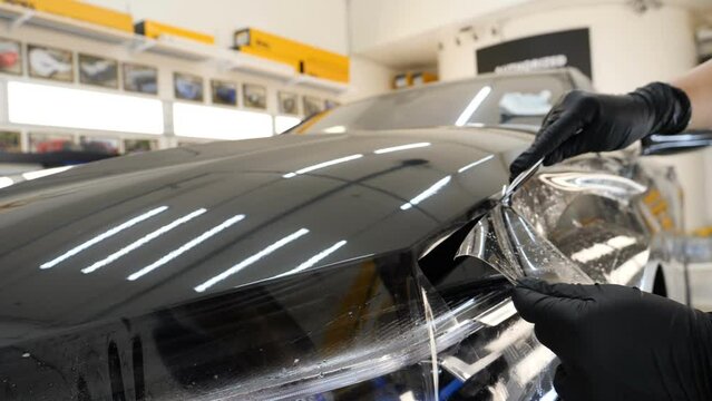 Close up to PPF installation process on a front headlight and hood. PPF is a Paint Protection Film which protect paint from scratches and stone chips. Concept of: Guard, Protect, Car, New, Work.	
