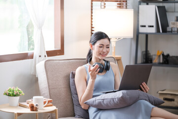 Young smiling happy beautiful asian woman relaxing using laptop computer in the livingroom at home.Young creative girl working and typing on keyboard.work from home concept