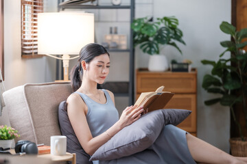 Happy young woman reading book on sofa at home. Lifestyle freelance relax and chill drinking coffee in living room. Lifestyle Concept
