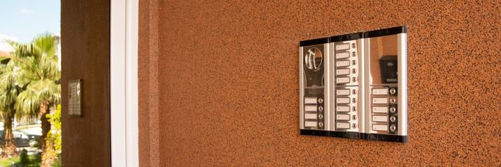 Entrance doorbell in multi-apartment building, with intercom device, on brown wall