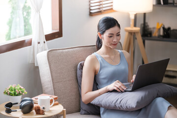 Young smiling happy beautiful asian woman relaxing using laptop computer in the livingroom at home.Young creative girl working and typing on keyboard.work from home concept