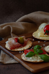 Set of appetizers - crackers with cheese, salami, prosciutto, tomato, olives and salad on dark brown background 