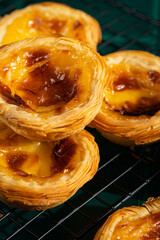 Group of four traditional Portuguese pastel de nata on cooling wire rack on green tiled surface.