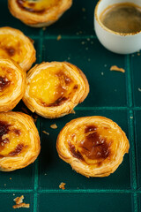 Group of traditional Portuguese pastel de nata and cup of espresso on green tiled surface.