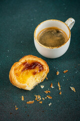 Single bitten pastel de nata (traditional Portuguese custard pastry) and cup of espresso on green surface.