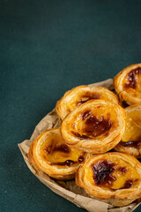Pile of traditional Portuguese pastel de nata on paper bag in dawn right corner on green surface.