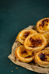 Pile of traditional Portuguese pastel de nata on paper bag in dawn right corner on green surface.