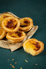 Pile of traditional Portuguese pastel de nata on paper bag on green surface.