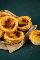 Pile of traditional Portuguese pastel de nata on paper bag on green surface.